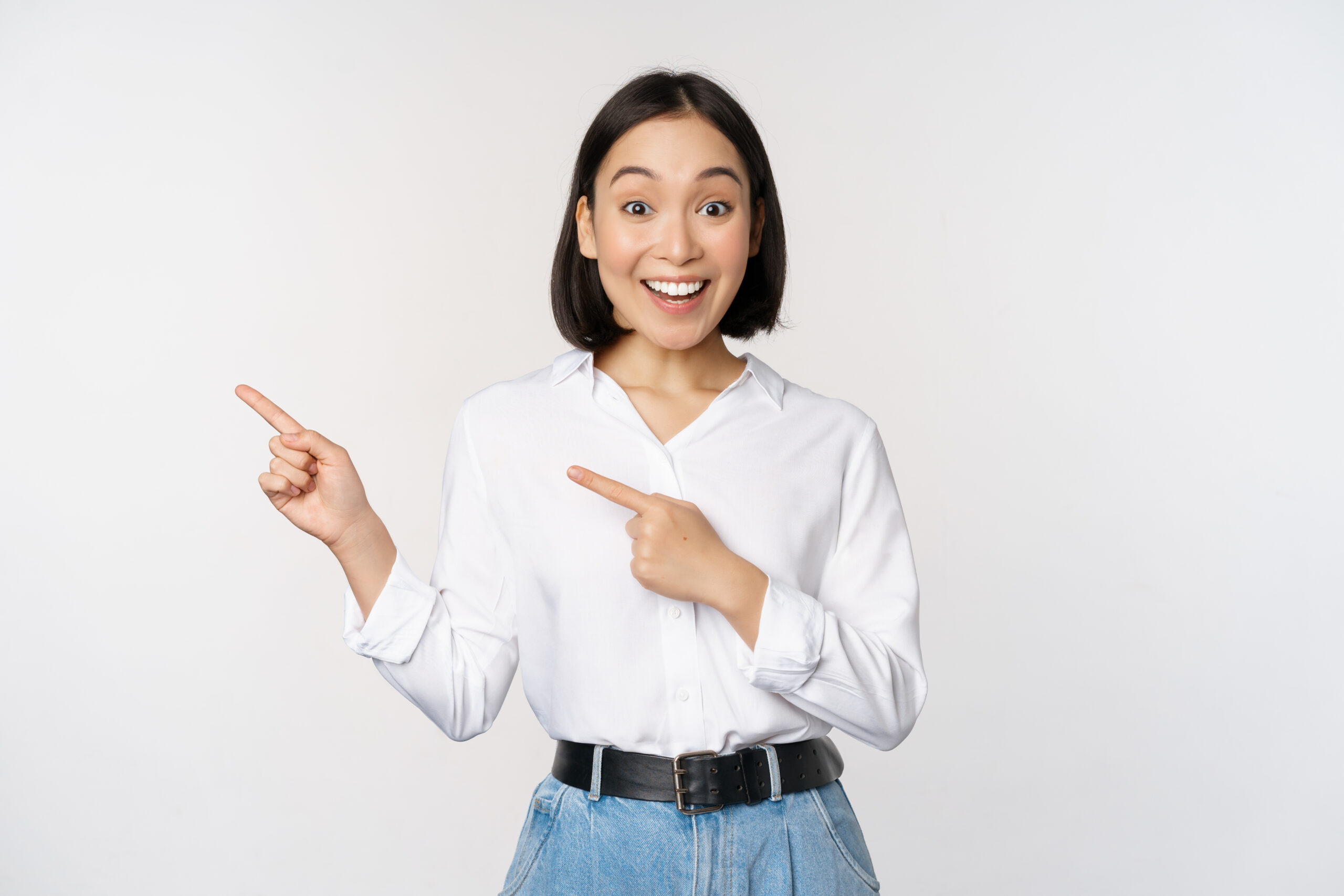 portrait of excited young asian woman, office lady pointing fingers left at discount, showing sale banner, standing over white background